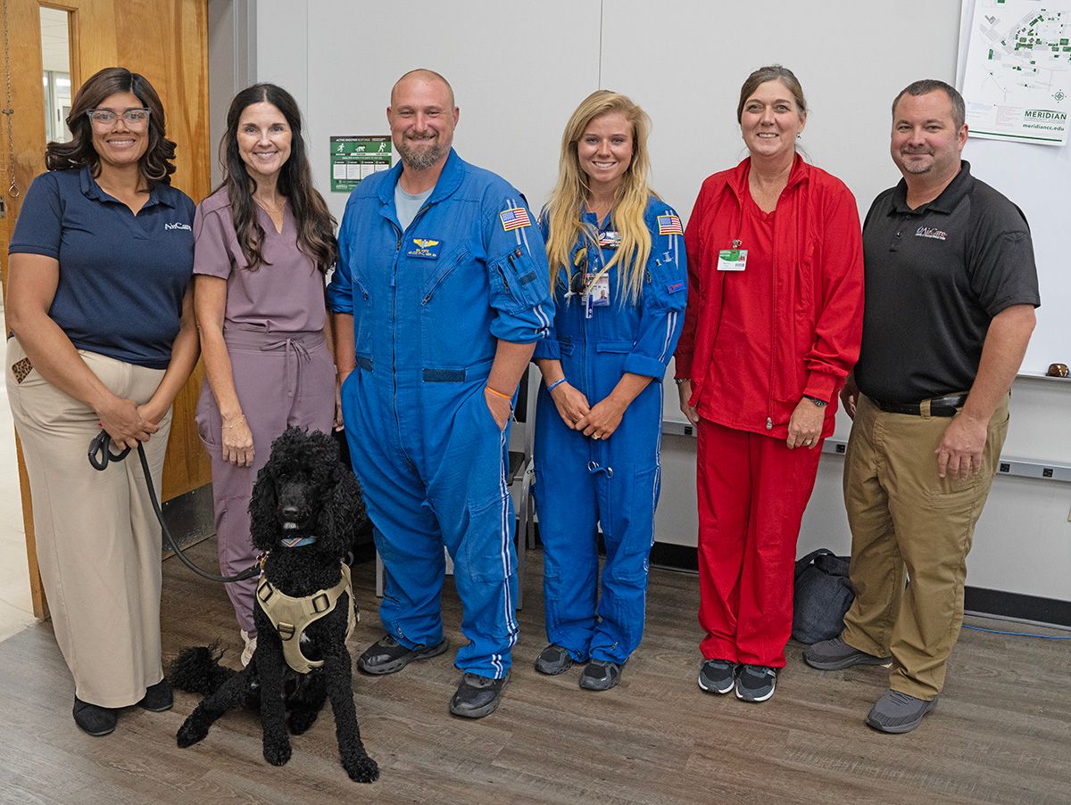 Gathering after the presentation are from left, Kawanna McCormick, health systems operations manager; Tara Coody, MCC Associate Degree Nursing Program instructor; Ben White, critical care paramedic; Ally Westrope, flight nurse; Don Moore, base supervisor for Meridian and critical care medic; and Melanie Pinter, MCC Associate Degree Nursing Program instructor. Seated is Aero, GMR therapy dog.  