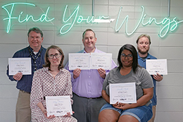 Tony Boutwell, Kay Thomas, Matthew Milner, Tanisha Clark, and Hunter Heath pose with award certificates in front of a neon green 