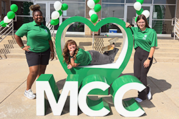 Ivy League Recruiters pose in front of large green heart and MCC letters.