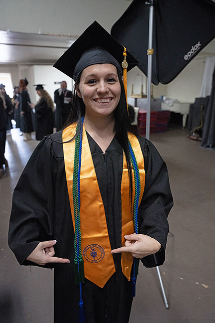 In her graduation attire, Destiny Redmond proudly points to her Phi Theta Kappa stole. Redmond earned her associate of applied science degree and three certificates at the conclusion of the Fall Semester 2023.  