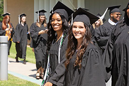A group of students in their caps and gowns walk down the sidewalk of the MCC campus. 