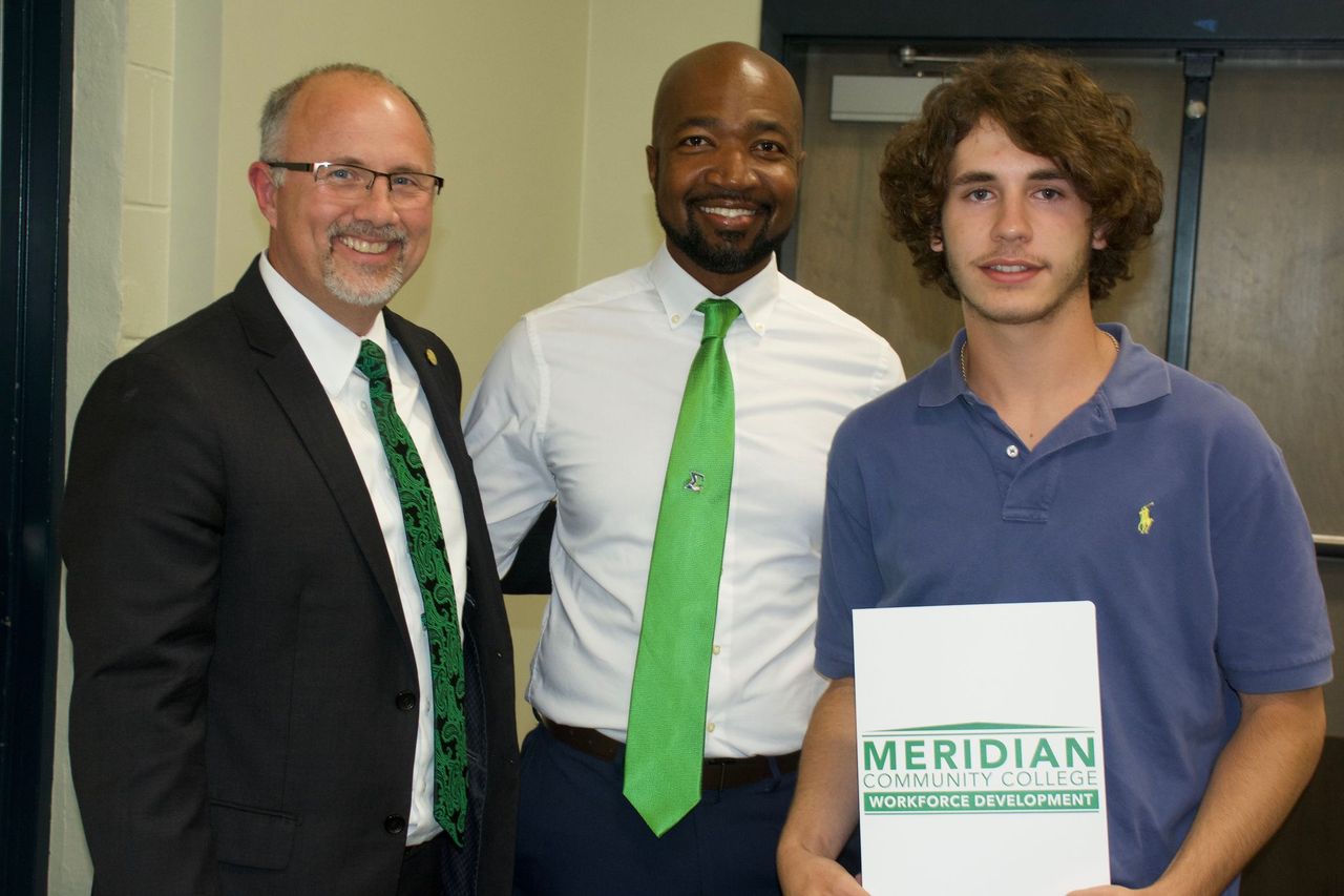 MCC President Dr. Thomas Huebner, left, and Utility Lineman Program Instructor Curtis Bradley, center, congratulate student Drew Adkinson during a completion ceremony. 