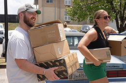 Two students carrying boxes and smiling.