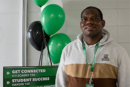 Student stands in front of green and white balloons. 