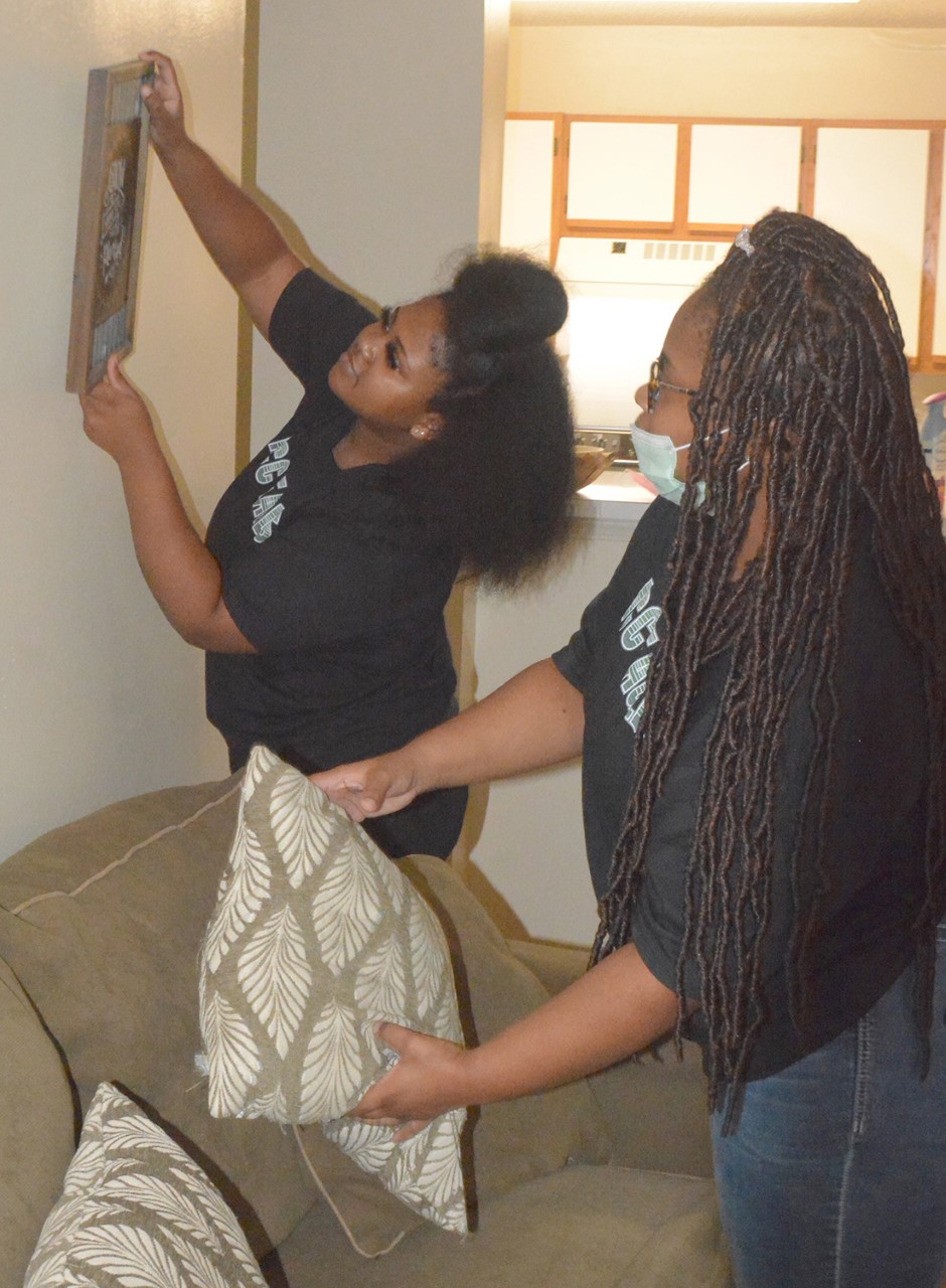 Residence Assistants Tywonna Clemons, left, and Ariel Coburn adjust a framed artwork in their College Crossing Apartment.